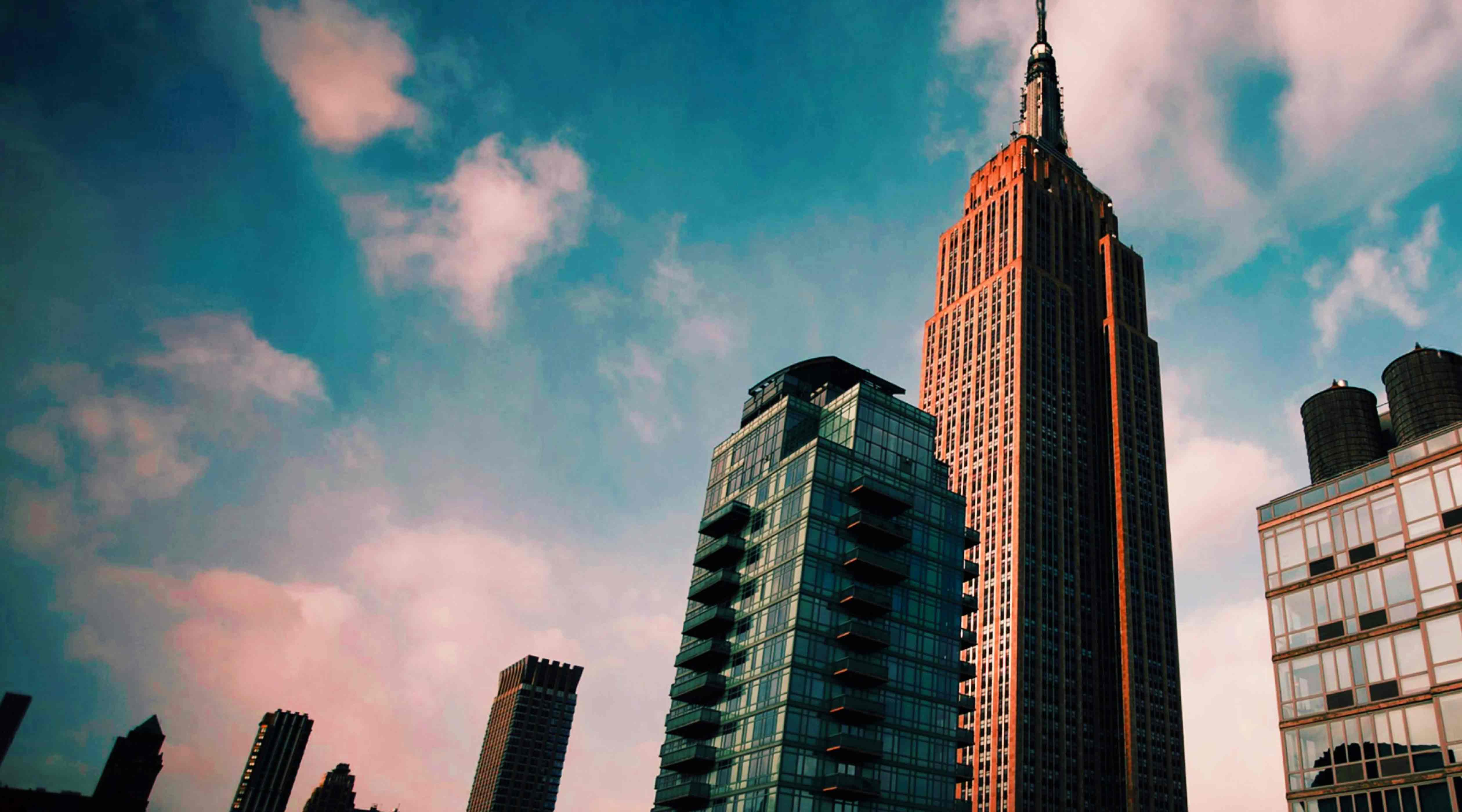 Empire State Building and nearby glass high-rises under a blue sky with pink clouds, representing StrawberryFrog's creative marketing & brand strategy offices in New York.