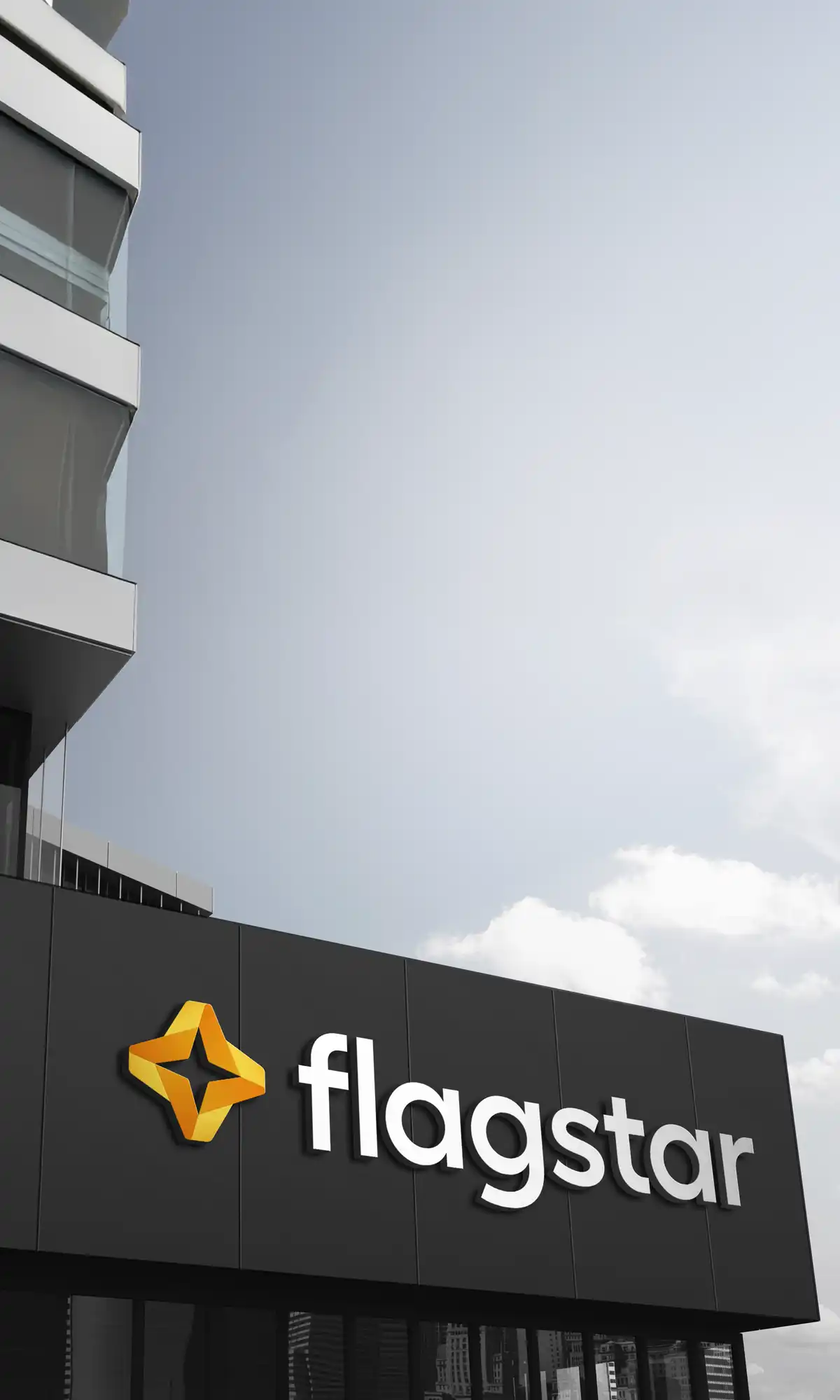 Modern building facade with dark gray vertical paneling featuring the Flagstar logo - an orange and yellow star with folded ribbon design - and white raised lettering spelling "flagstar" against a blue sky with scattered clouds.
