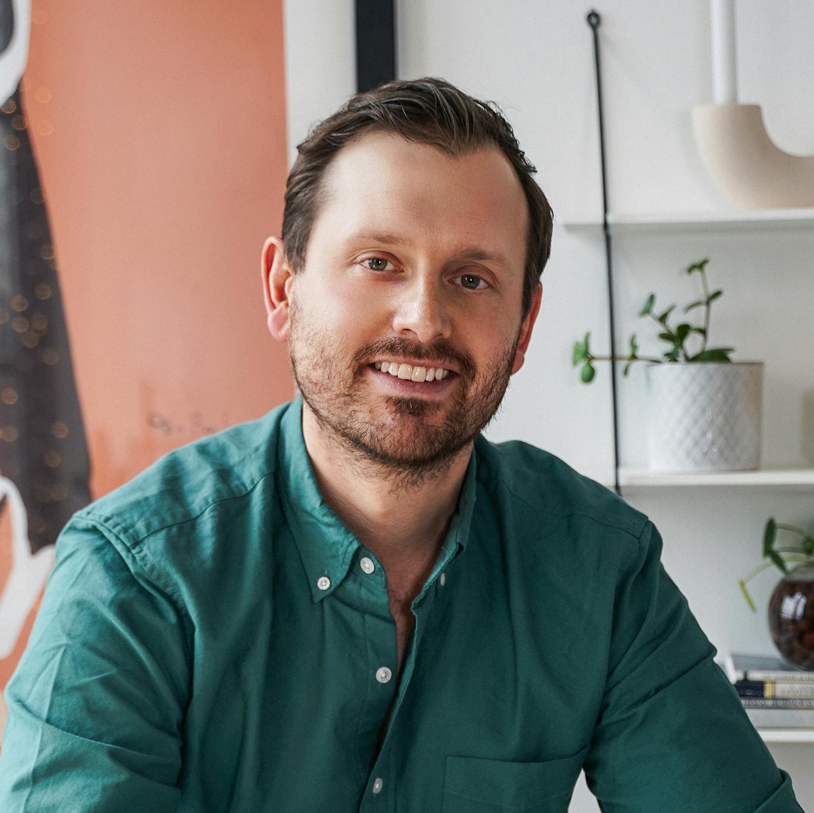 Portrait of StrawberryFrog Managing Director Dan Langlitz wearing a green button-down and smiling in front of a minimalistic background.
